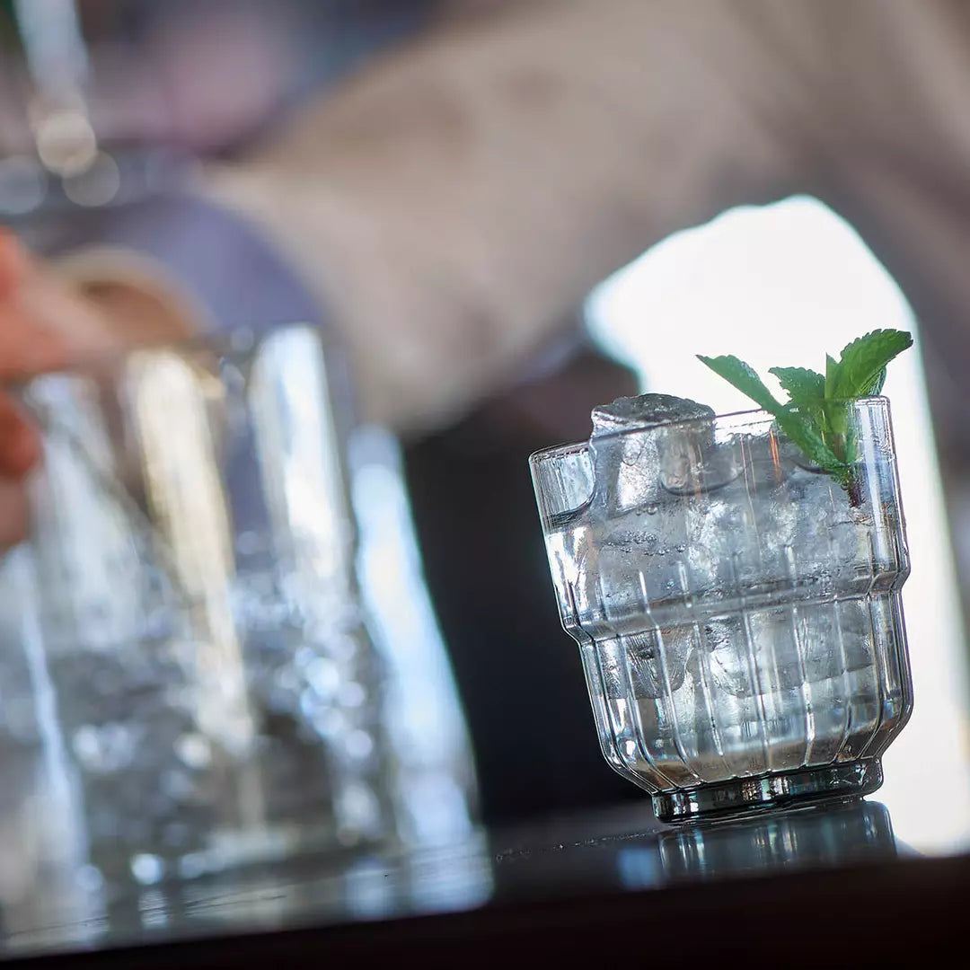 Clear glass with a textured base and a sprig of mint on a blurred bar background
