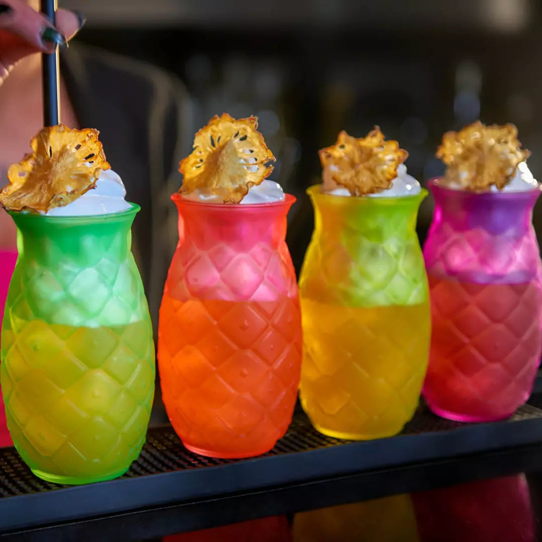Four colorful drinks in pineapple-shaped glasses with a blurred background