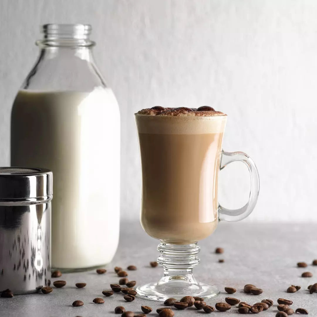 Glass mug of coffee with a bottle of milk and coffee beans on a light background