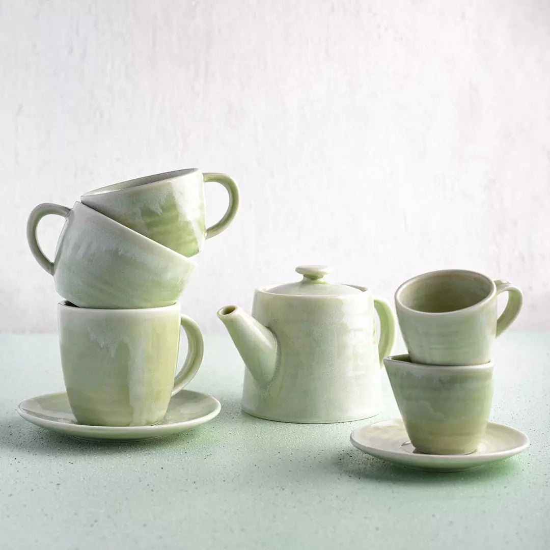 Stacked coffee and tea cups with teapot on light blue background