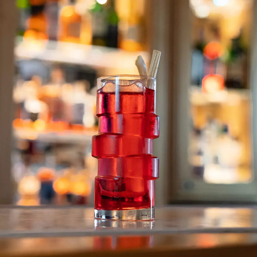 Red cocktail in a glass with ice cubes on a bar.