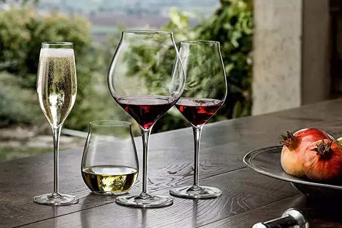 Four different glasses with liquid on wooden table with fruit bowl in picture