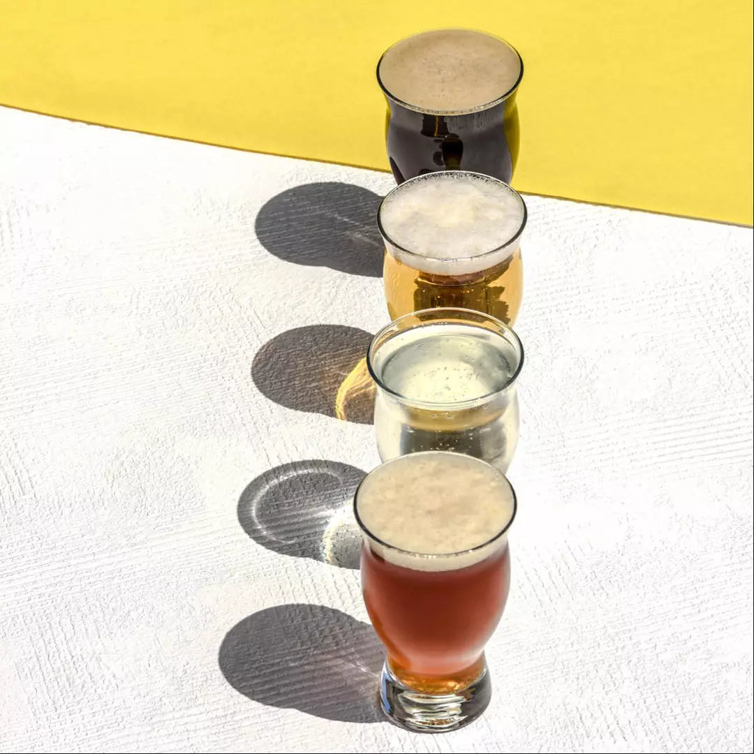 Four draft beer glasses with different coloured liquids on a white/yellow backgrounf