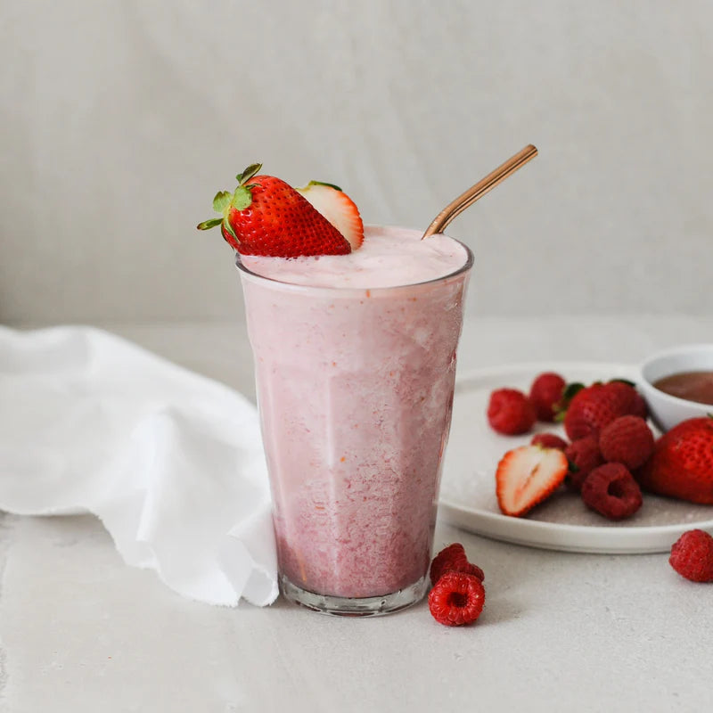 Strawberry and raspberry smoothie with a gold straw on a light surface with strawberries and raspberries.