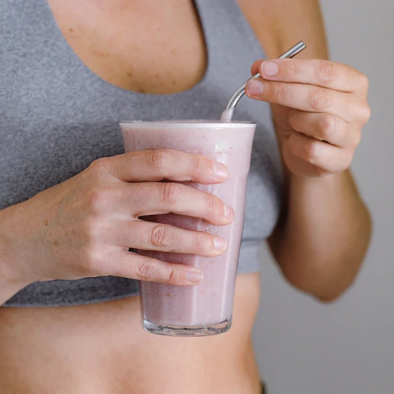 Person holding a pink smoothie with a straw against a neutral background