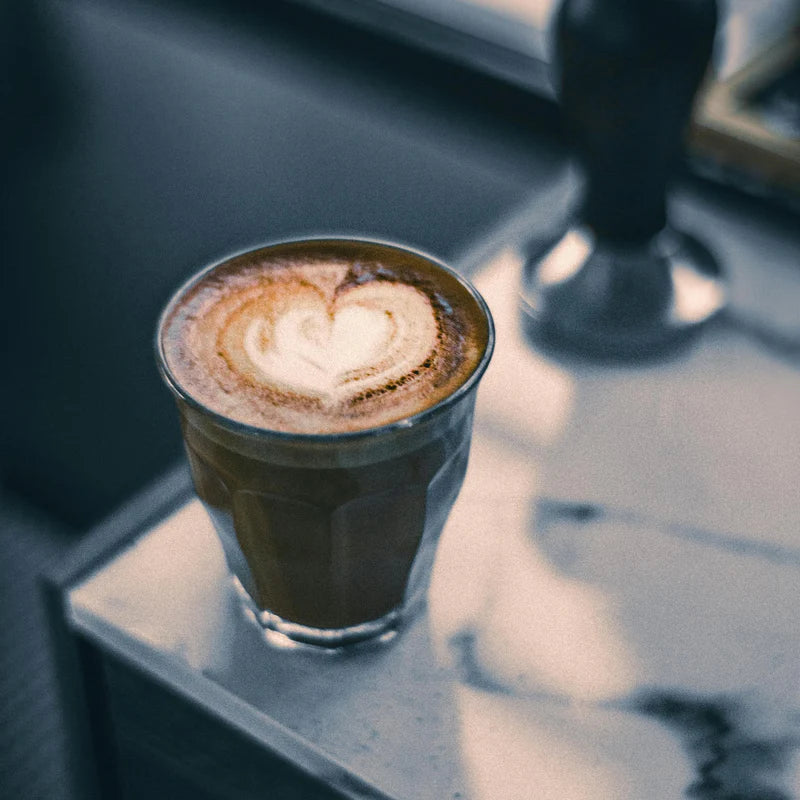 Cappuccino with a heart-shaped foam design in a glass cup on a marble surface.