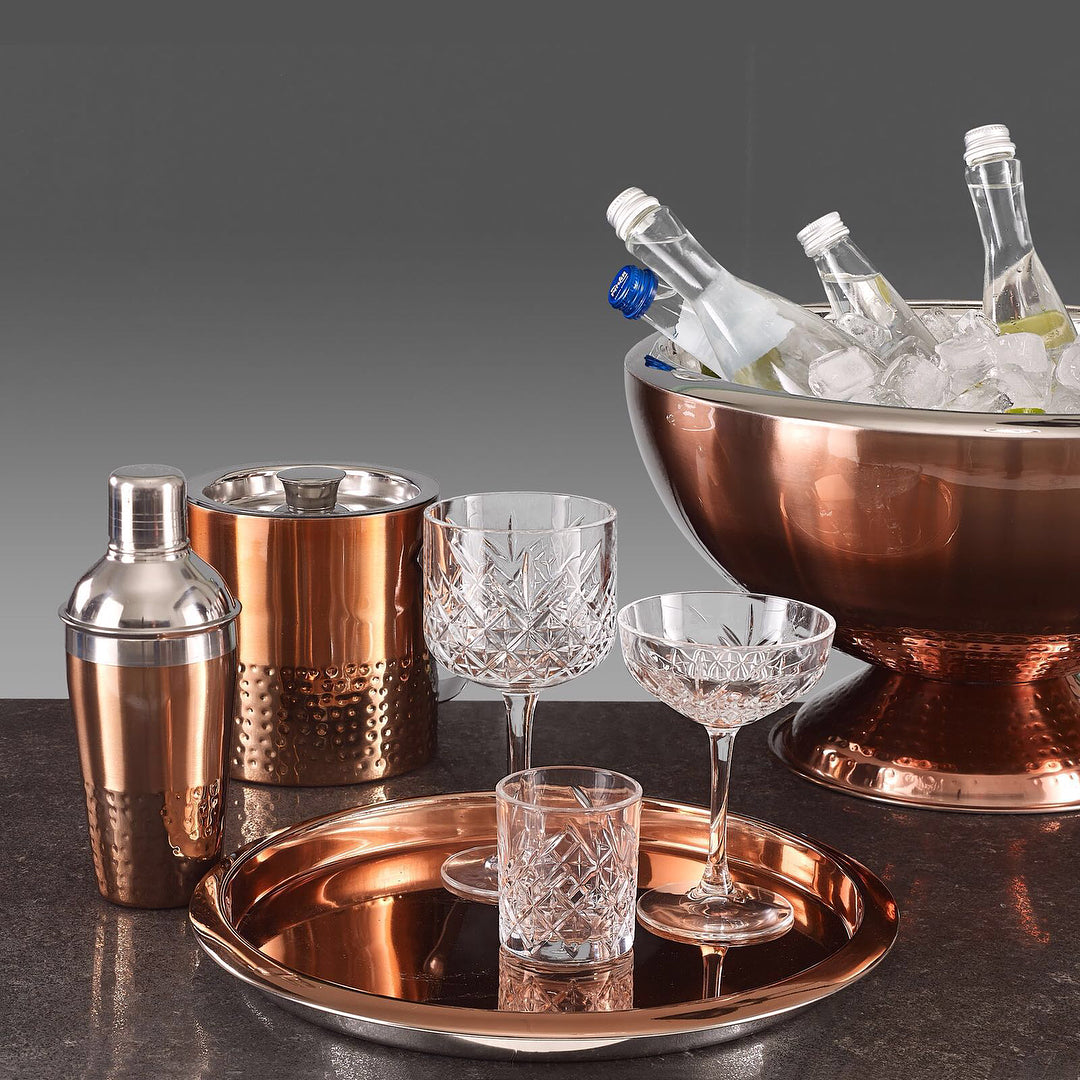 The clear glasses on copper tray with bar accessories in background
