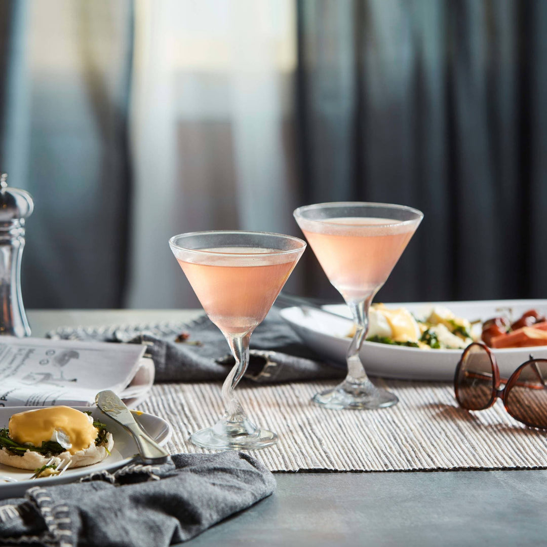 2 Z Stemmed Martini glasses with pink liquid in each on a table setting with a plate of food
