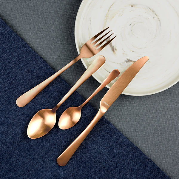 Four piece copper cutlery set on white plate with blue table cloth background