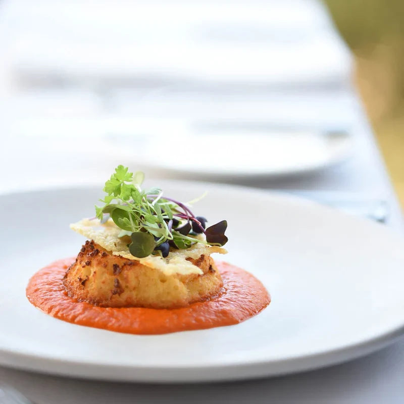White coupe plate displaying a tomato base and fish cake and condiments