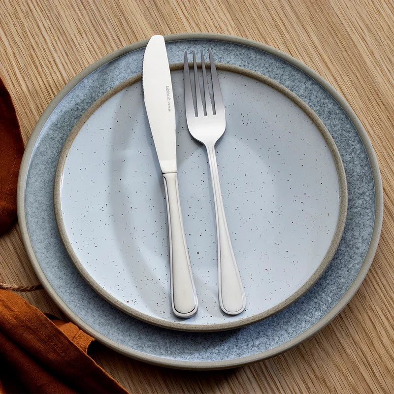 Set of silver knife and fork on a gray ceramic plate with a wooden background