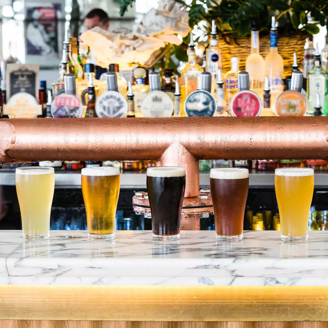 Five different schooner glasses with different coloured liquids on a bar setting