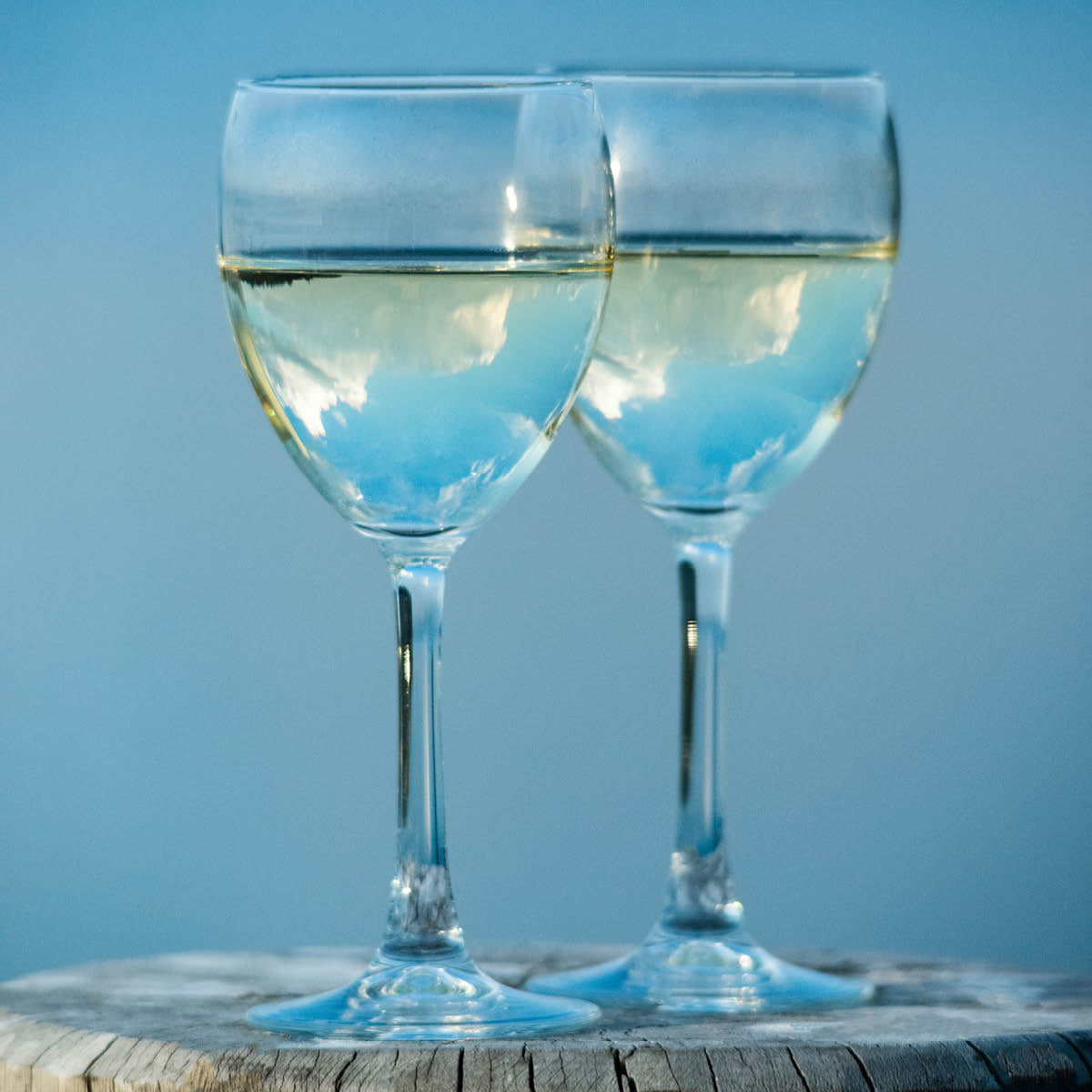 Two white wine glasses with liquid on sky blue background