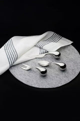Three polished metallic utensils, including a fork, spoon, and a small knife, arranged on a round gray felt placemat with a white cloth napkin featuring gray stripes, set against a solid black background.