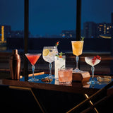 Six different geometric cocktails glasses on a serving table with a city skyline in the background