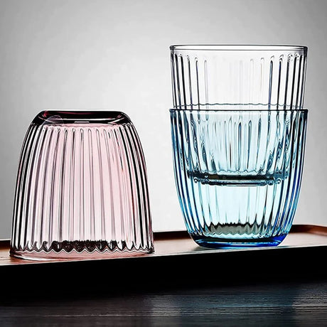 Two ribbed glass tumblers, one pink and one blue, on a wooden surface with a gray background.