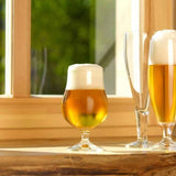 Three beer glasses - 2 with liquid, one clear on a table with a window background