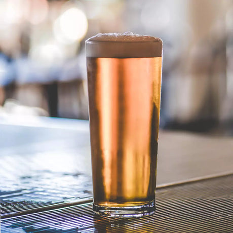 Tall Schooner sized beer glass with liquid presented on a blurred bar background