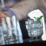 Clear glass with a textured base and a sprig of mint on a blurred bar background