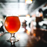 Large Belgian beer glass with liquid on a blurred bar / pub background
