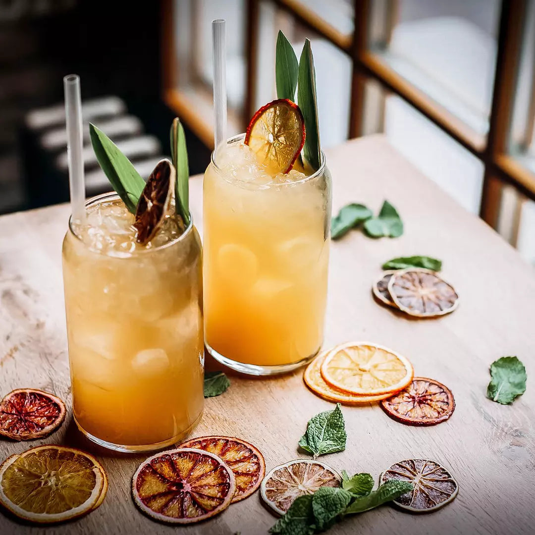 Two beer can shaped glasses with liquid and garnish on a table with dried lemons
