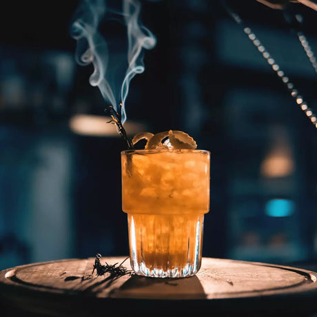 Cocktail with ice and a smoking herb on a wooden surface with a blurred background