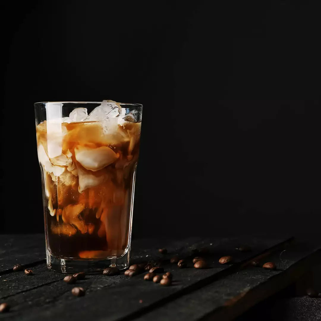 Glass of iced coffee on a table with coffee beans scattered around