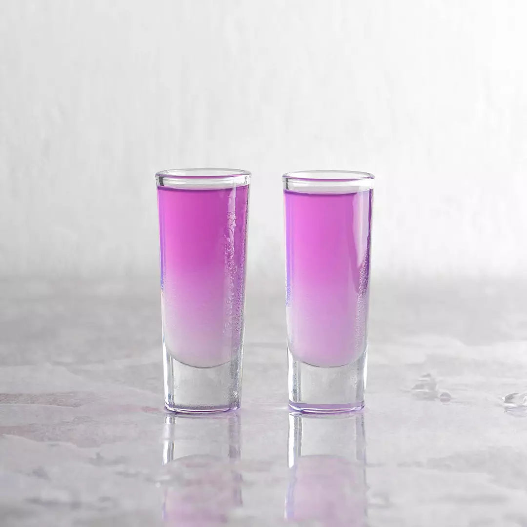 2 shot glasses with pink coloured liquid on a marble background