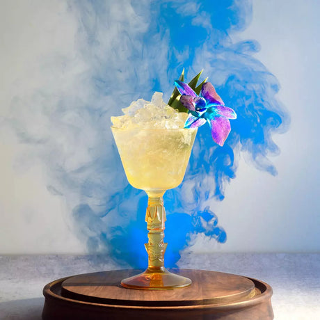 Decorative coupe glass with yellow liquid on smokey sky blue background