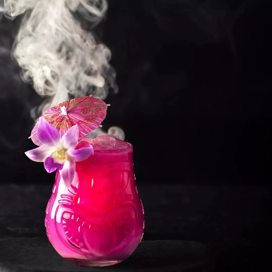 Pink cocktail with flowers and an umbrella on a dark background