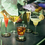 A range of geometric glasses - all with liquid displayed on a bar setting with a barman in the background