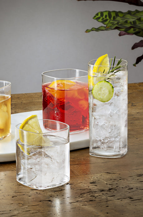 Two small square tumblers both with liquid and one large square highball glass with liquid and garnish presented on a table setting