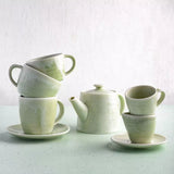 Stacked coffee and tea cups with teapot on light blue background