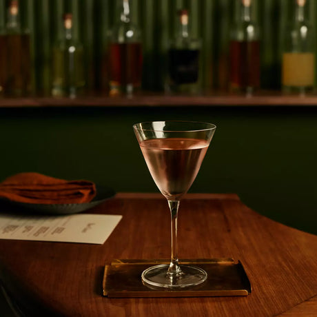 Cocktail glass with a drink on a wooden coaster in a bar setting