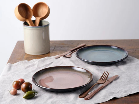 Two medium sized dark round plates with matching cutlery on a table setting with olives at front of photo