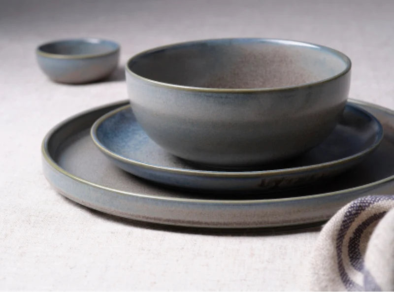 Four different sized bowls and plates in a grey / blue colouring presented on a light grey background