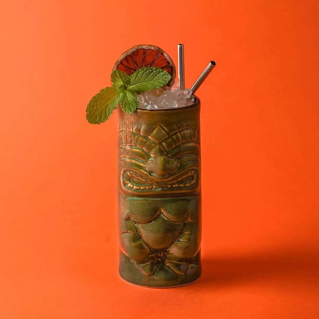 Cocktail in a tiki mug with ice and mint leaves on an orange background