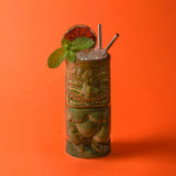 Cocktail in a tiki mug with ice and mint leaves on an orange background