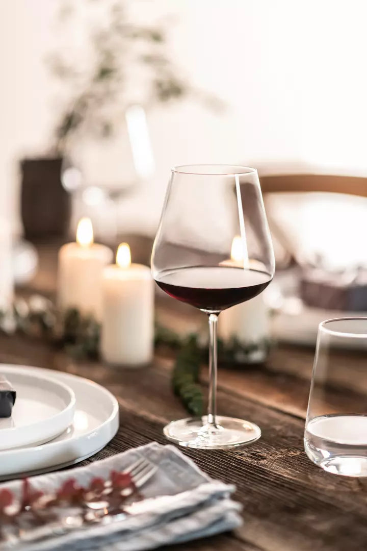 Large red wine glass with burgundy coloured liquid on a table setting with white plates and a water glass