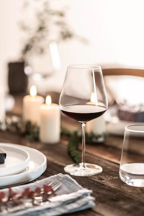 Large red wine glass with burgundy coloured liquid on a table setting with white plates and a water glass