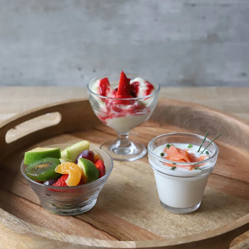 Three different dessert cups all with fruit salad and yoghurt displayed on a wooden tray