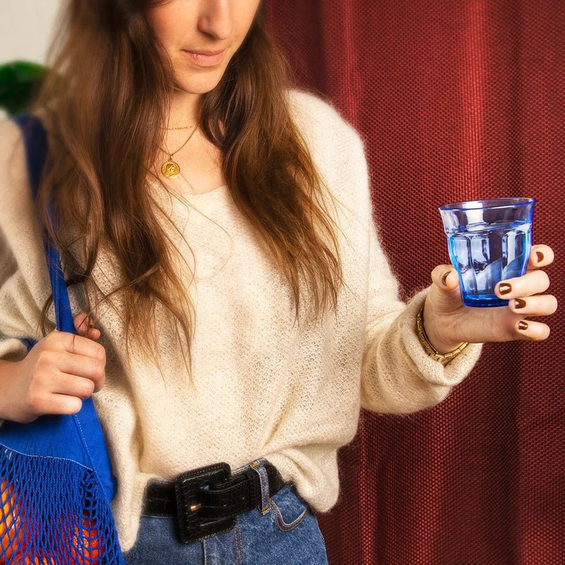 Woman holding a blue glass and a blue bag against a red curtain background
