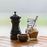 A wooden salt and pepper shaker, with sugar bowl and teaspoon on a table setting outside