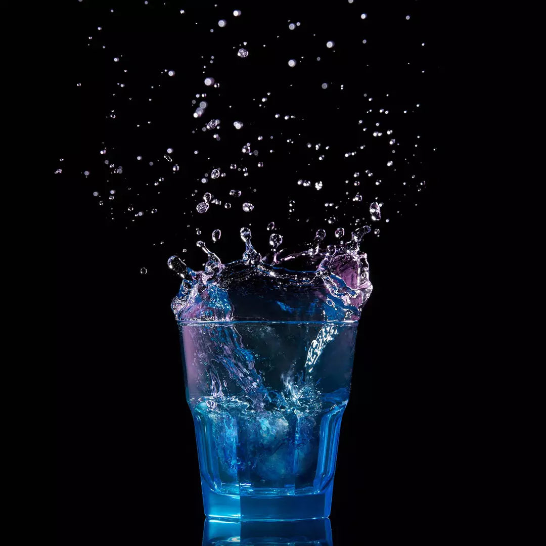 Blue liquid splashing out of a glass against a black background