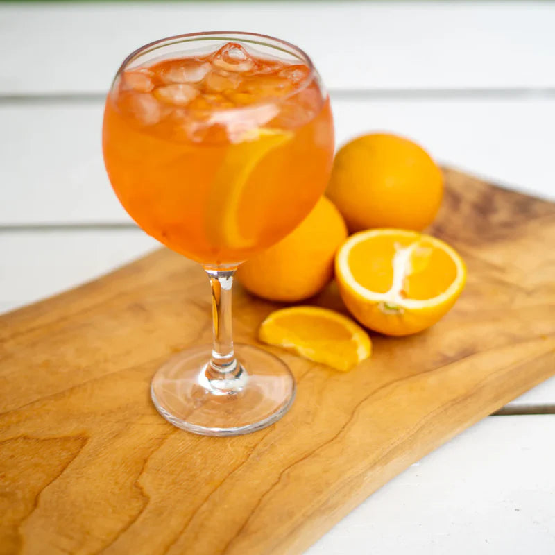 Glass of orange cocktail with ice and oranges on a wooden board in ballon glass.