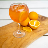 Glass of orange cocktail with ice and oranges on a wooden board in ballon glass.