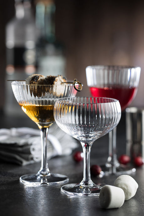 Three different lined champagne and cocktail glasses presented on a blurred bar scene background
