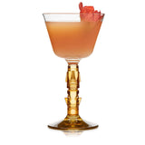Coupe glass with orange liquid and flower on white background