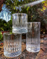 Three Pasabahce Elysia glasses grouped on a stone surface outdoors — two short whisky tumblers and one tall glass showing vertical and diamond-cut detailing