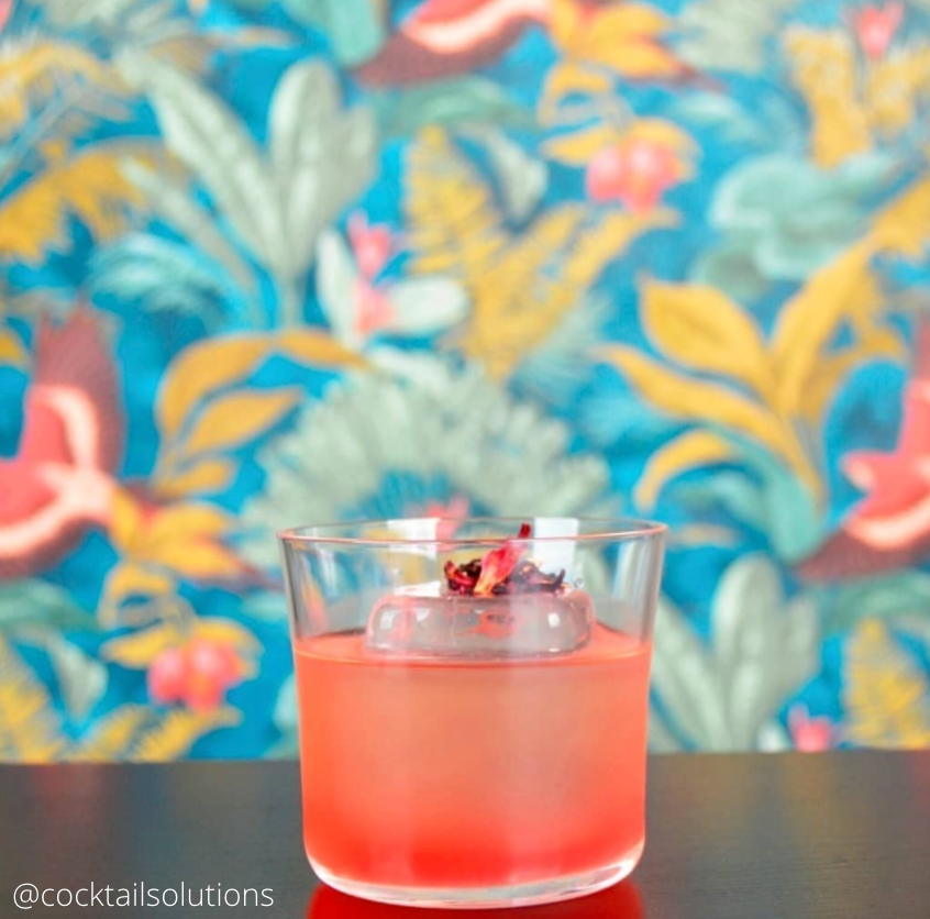 Small water glass with pink liquid on floral background